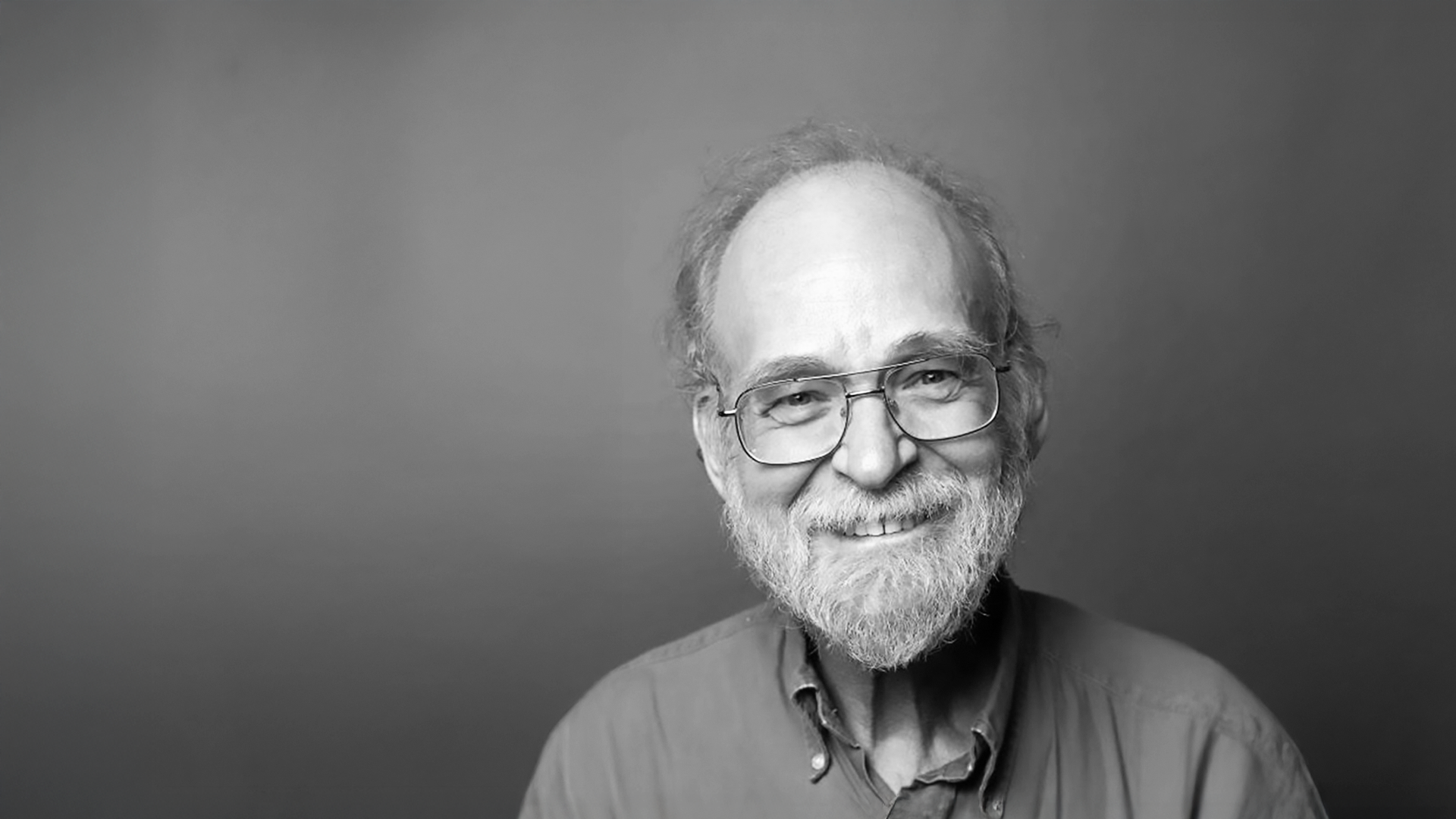 A black and white photo of a man with glasses and a beard.