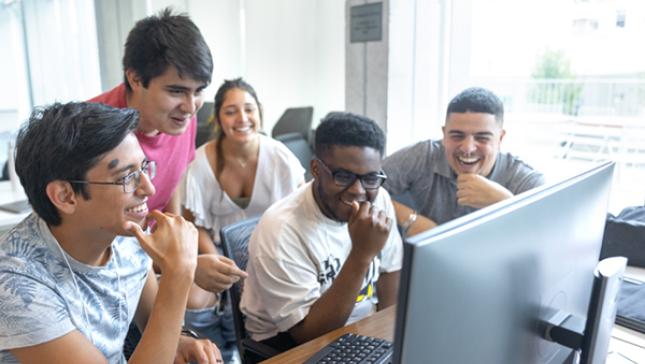 Students work together and laugh facing a computer.