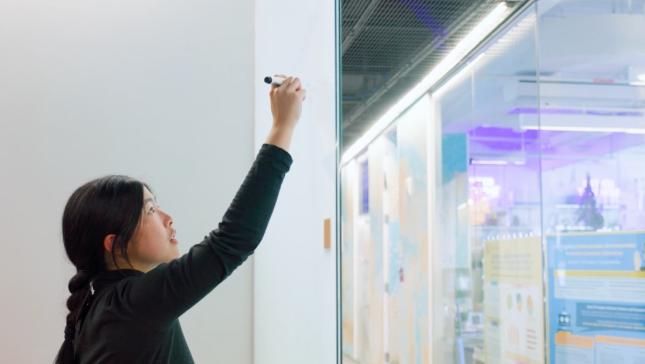 woman with hair in braid writing on white board