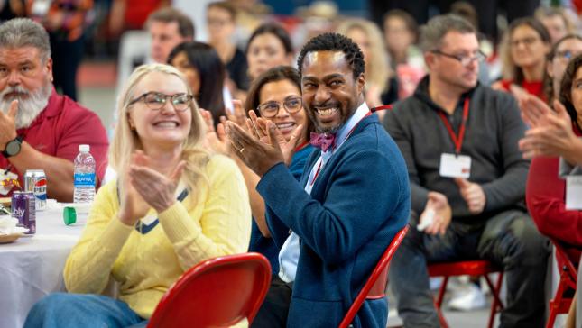 a group of people sit in chairs around tables clapping