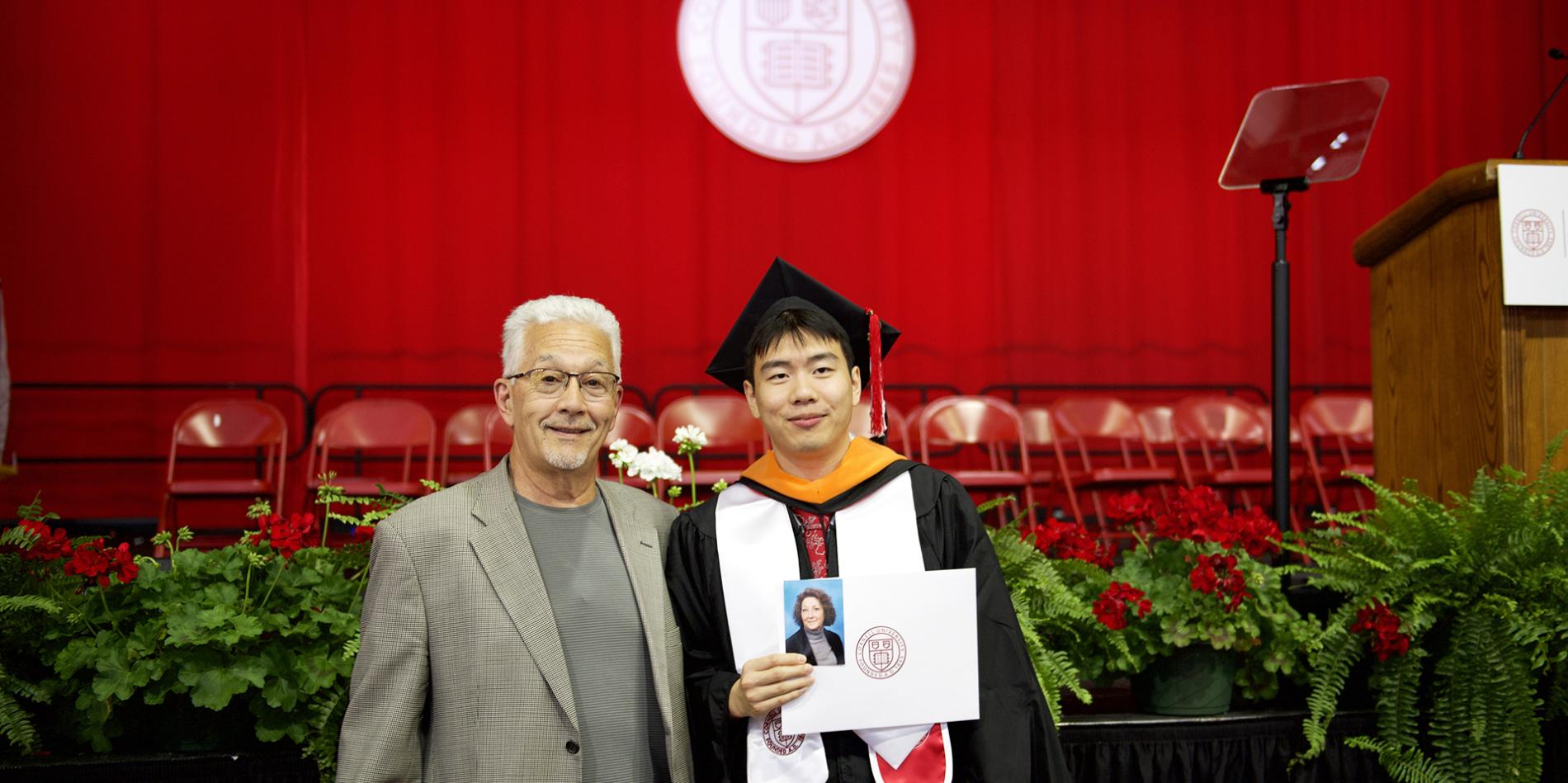 A color photo of a recent graduate in regalia with a family member.