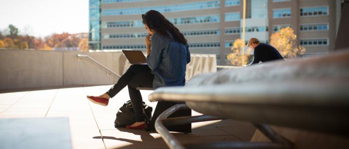 a female student with long brown hair sits on a chair outside gates hall