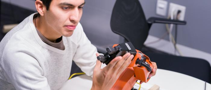 a male student with tan skin and dark black hair touches an orange robot