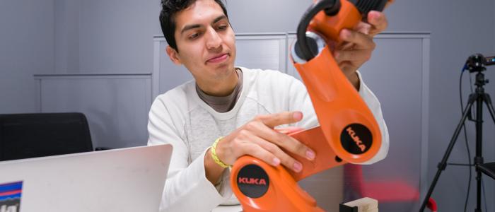 A man manipulates an orange robot orange next to a laptop