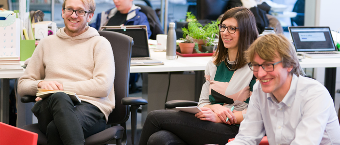 Graduate students sitting and smiling during a group discussion in an office space.