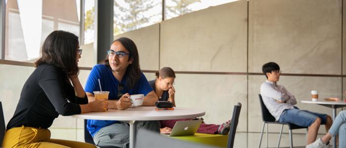 Students sitting and talking at tables in a campus café area.