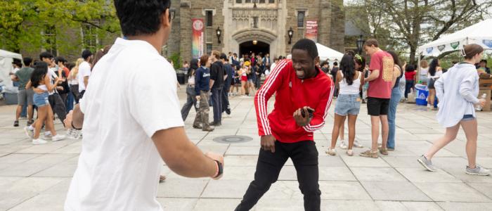 Two students dance in a courtyard in front of a stone academic building