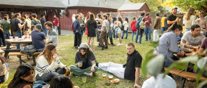 Dozens of grad students sit and stand on a green lawn in front of a red barn.