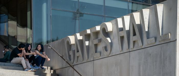 two students sit on the gray steps of Gates hall tallking