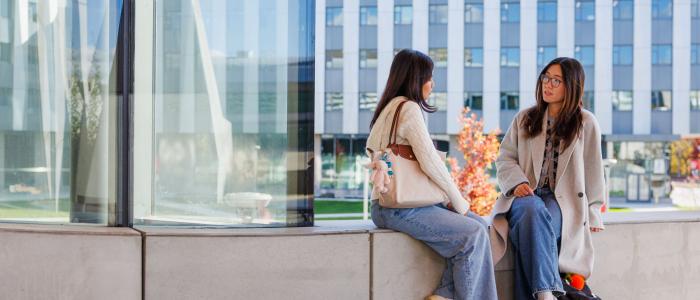 two students sit on ledge outside Gates Hall