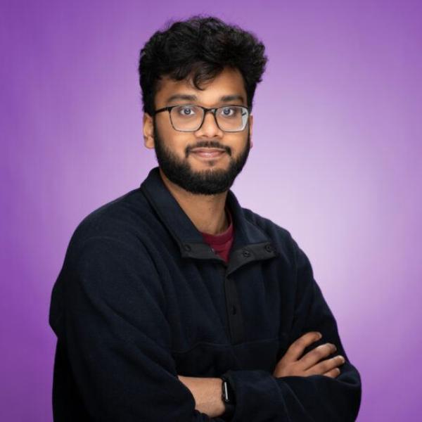 A color portrait of a man with glasses in front of a purple background.