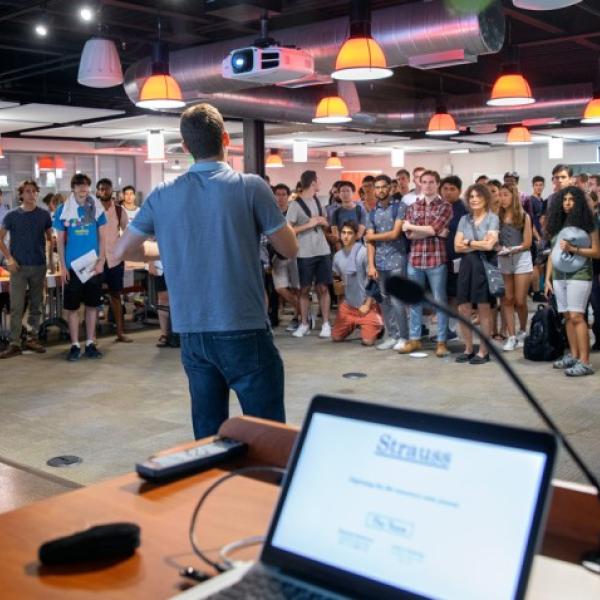 wide view of a room with a crowd of people listening to a man speak in the center