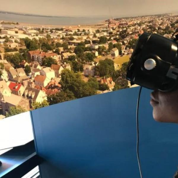 A participant wearing VR-type glasses with a visual of a sprawling suburb in front of them.