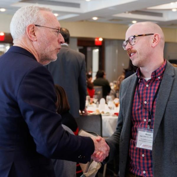 President Kotlikoff shakes the hand of a man with a mustache wearing glasses