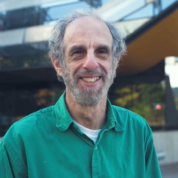 man in green shirt smiling in front of Gates Hall