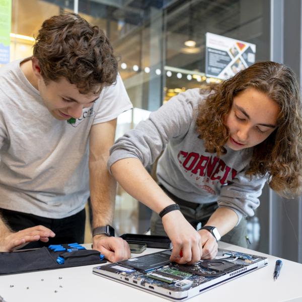 Two students tinker with a laptop.