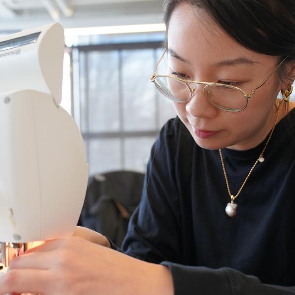 A woman in a black top sits and works on a sewing machine