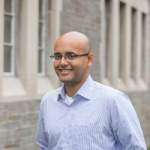 A color photo of bald man with glasses smiling at camera
