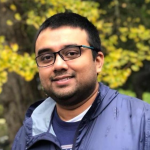 A color photo of Tapomayukh Bhattacharjee, a man with glasses, short dark hair and gray jacket