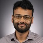 A photo of Eshan Chattopadhyay, a man with dark hair, a beard and glasses in a gray shirt.
