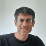 A photo of Robert Kleinberg, a smiling man with short gray hair, glasses and a black shirt in front of a gray background