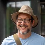 A photo of David Bindel, a man in glasses, a brown hat and blue tshirt
