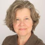 a women with gray-brown short hair smiles wearing a brown collared shirt