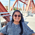 A color photo of a woman sitting outside wearing sunglasses.