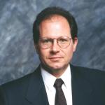 color portrait of man in suit, dark short hair, wire framed glasses