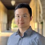 A photo of Kuan Fang, a man with glasses and dark hair in a gray shirt in front of a loggia. 
