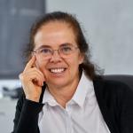 A photo of Éva Tardos, a woman with long brown hair, glasses, a white shirt and black cardigan