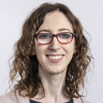 Women with glasses, curly hair, smiling at camera