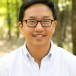 Portrait of a man in white shirt, dark hair and glasses. 