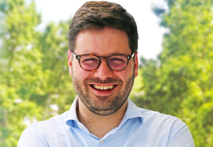 Color portrait of Andrew Owens, smiling at camera. He is wearing a blue shirt and glasses