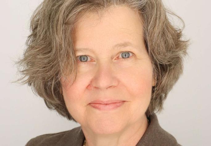 a women with gray-brown short hair smiles wearing a brown collared shirt