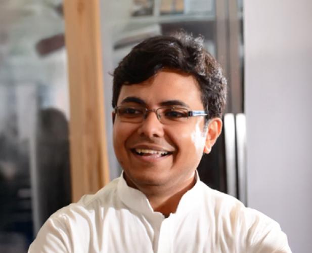 A photo of Karthik Sridharan, a smiling man with short dark hair, glasses and a white shirt