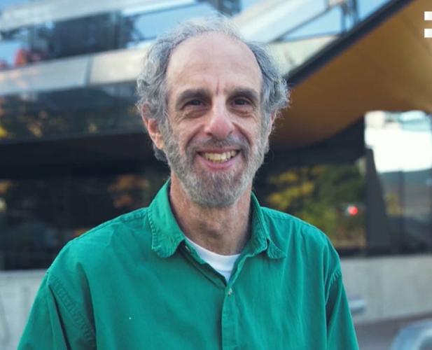 man in green shirt smiling in front of Gates Hall