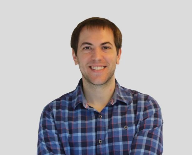 Man with short brown hair smiling at camera, wearing patterned shirt