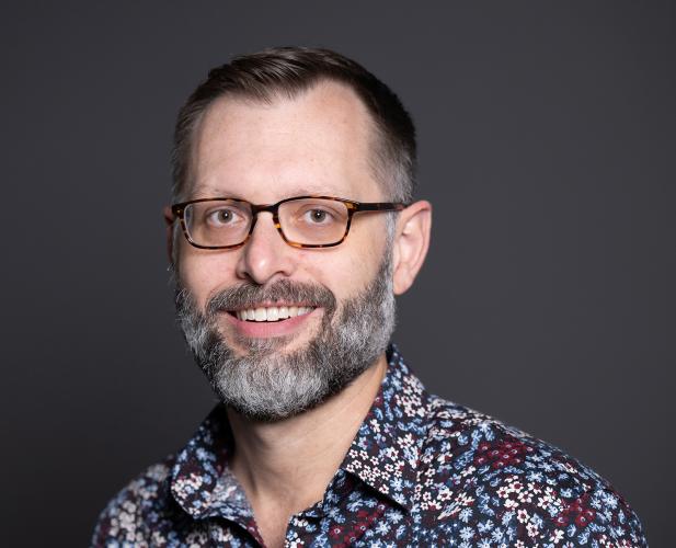 Portrait of man smiling at camera. he has on glasses and has a beard. 