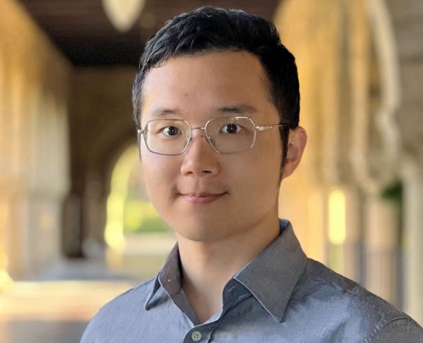 A photo of Kuan Fang, a man with glasses and dark hair in a gray shirt in front of a loggia. 