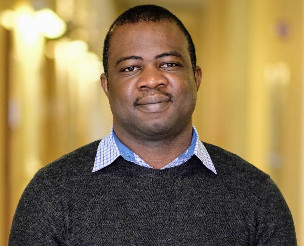 A photo of Owolabi Legunsen, a man with short black hair and mustache, in a black sweater in front of a gold background