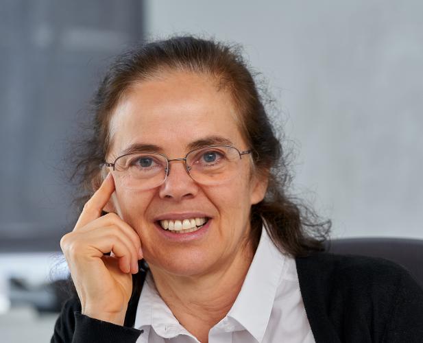 A photo of Éva Tardos, a woman with long brown hair, glasses, a white shirt and black cardigan