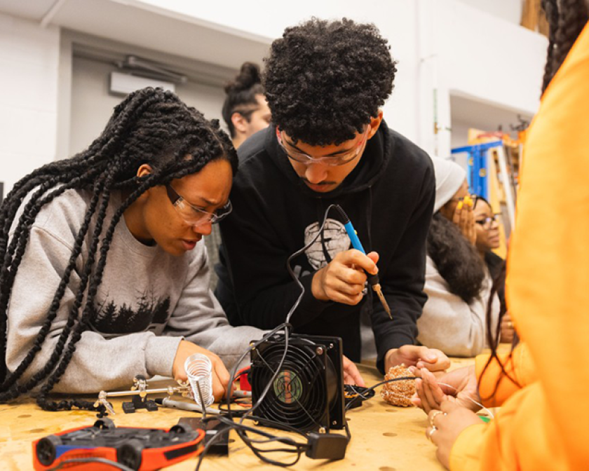 Students collaborating on an electronics project with soldering tools in a lab.