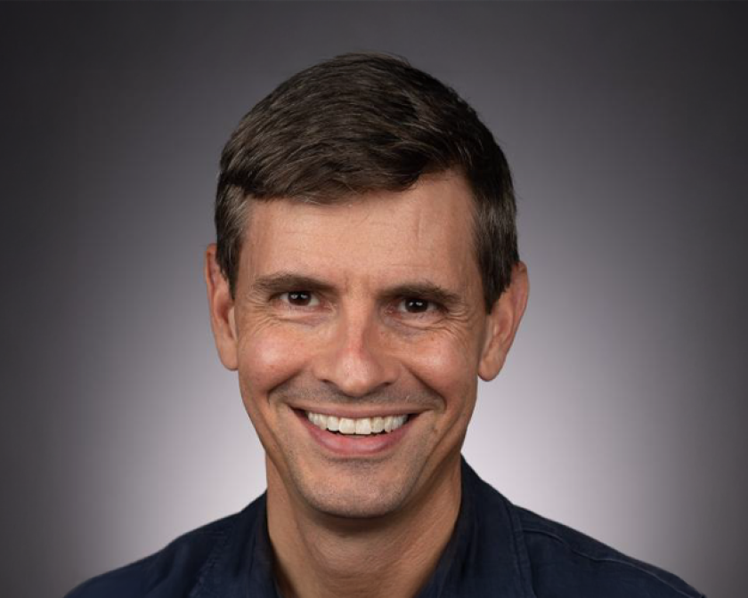 A color photo of a man smiling for a portrait.