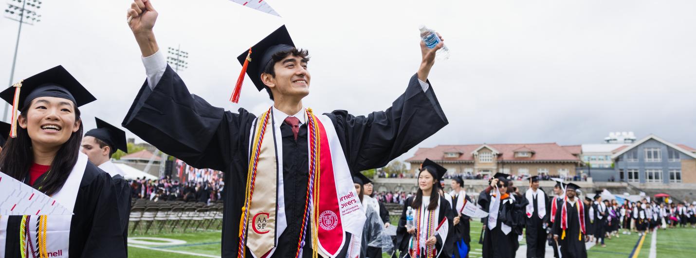 a student with graduation cap and flag waves on the field during commencement