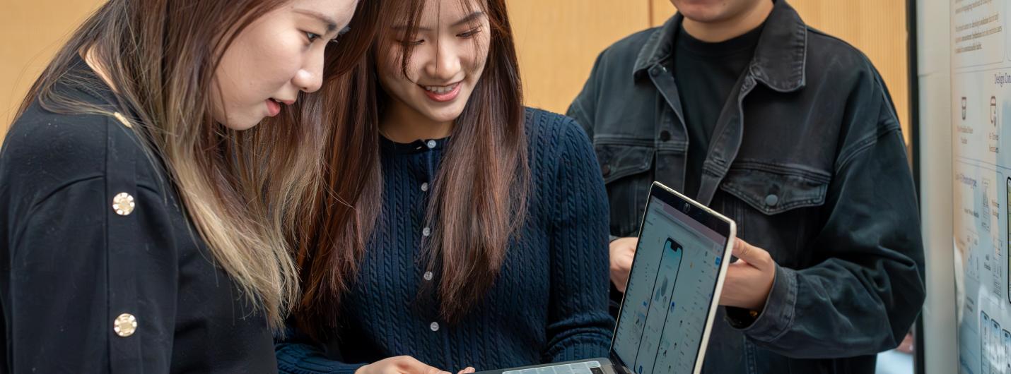 three students look on a lapptop