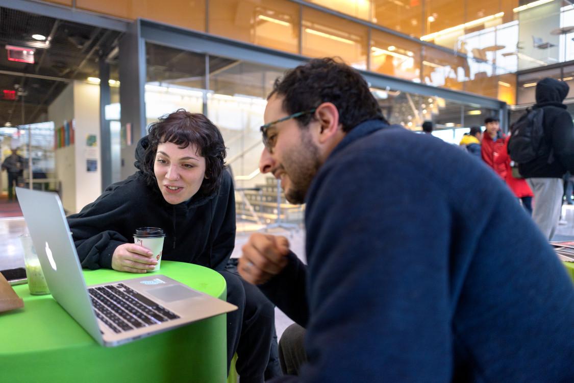  woman and man, both with dark hair, work on a laptop in Gates lobby